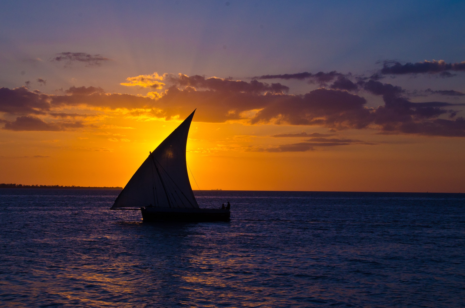 A traditional dhow sailing boat silhouetted against an orange sunset off Zanzibar, Tanzania